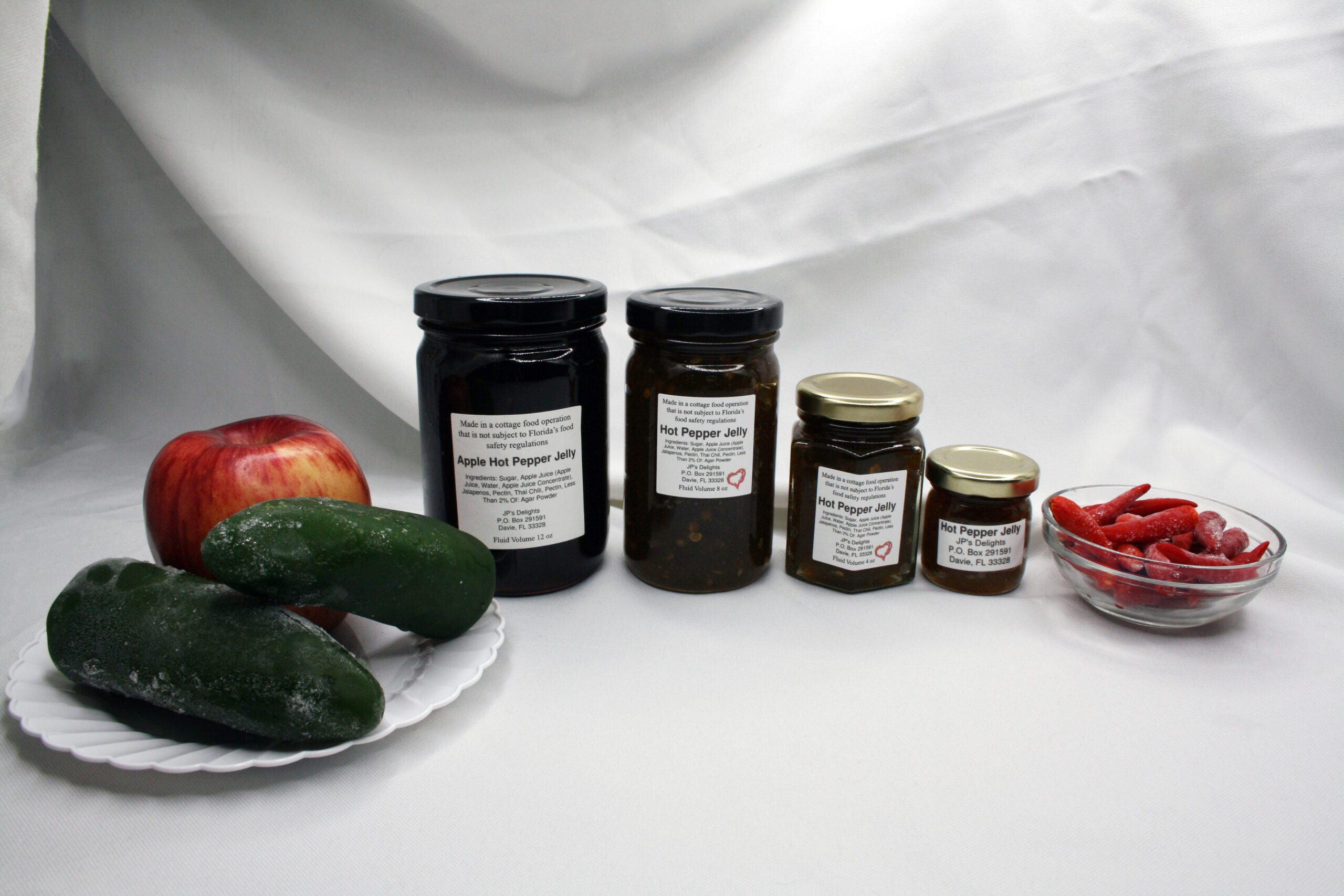 All 4 jar sizes of Apple Hot Pepper Jelly surrounded by its ingredients